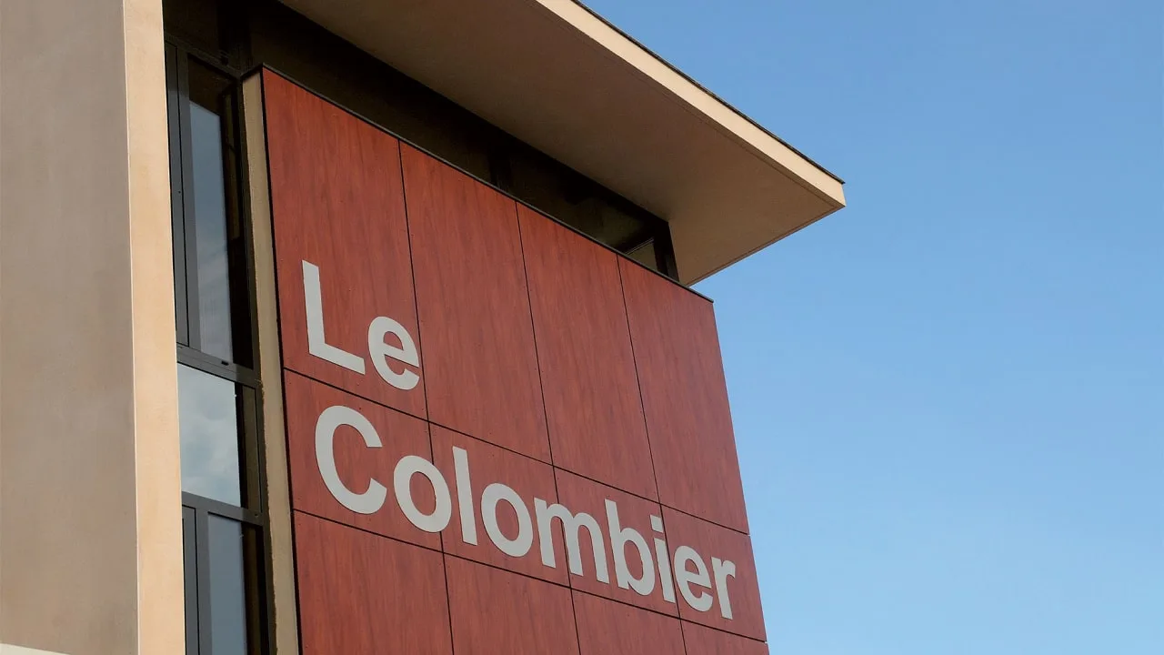 Gros plan d'un panneau en lettres blanches sur un bardage brun-rouge, sous un ciel bleu